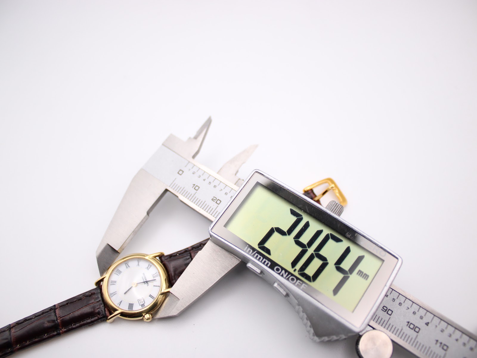 Digital caliper measuring the case diameter of the Raymond Weil 9940 watch, with the display showing a precise measurement of 24.64mm.