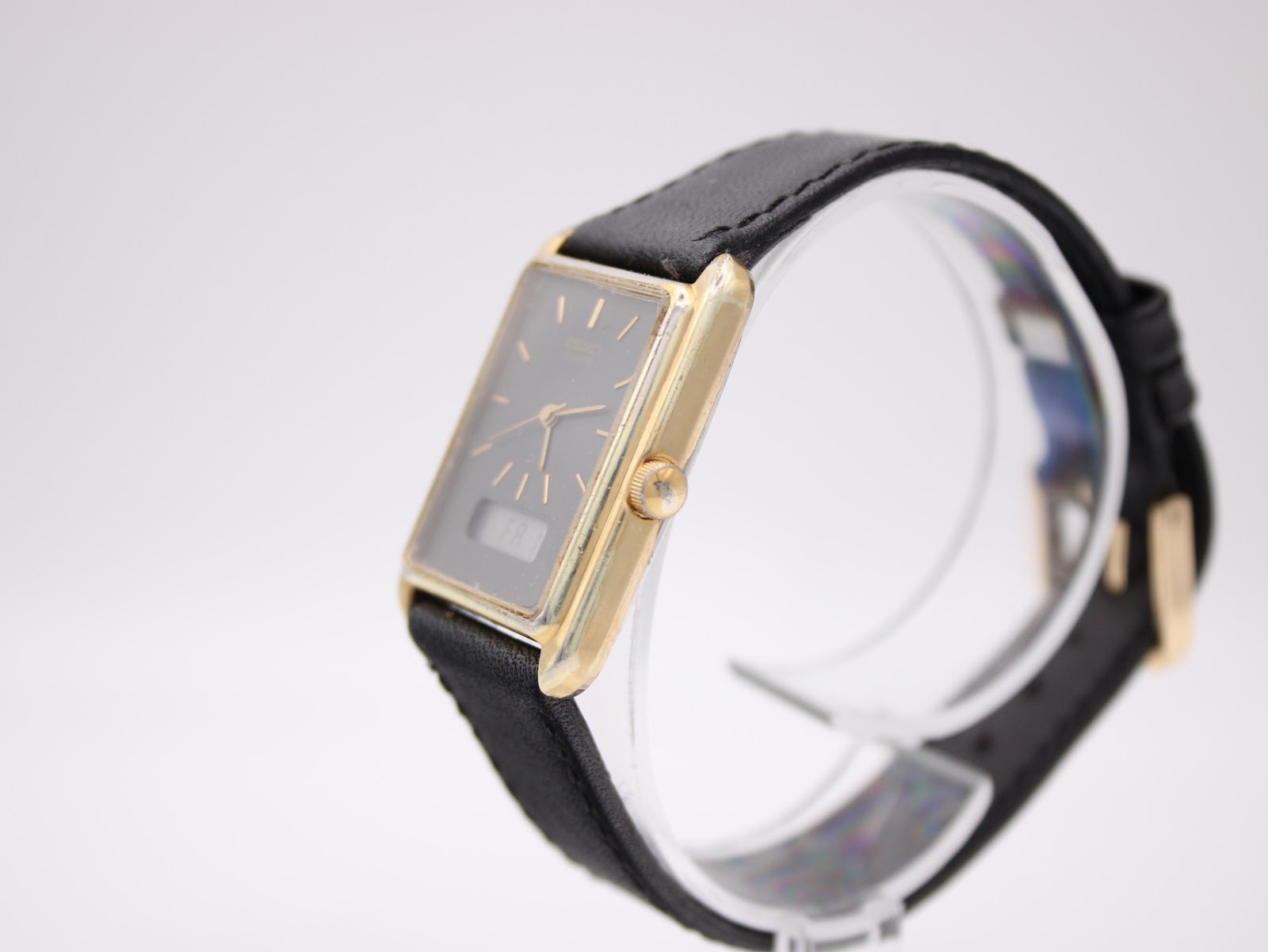 Angled side view of the Seiko watch on a clear stand, highlighting the gold-plated case profile and the crown.