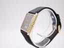 Angled side view of the Seiko watch on a clear stand, highlighting the gold-plated case profile and the crown.