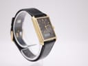 Three-quarter view of the Seiko watch on a stand, showing the full black leather strap and the sleek gold rectangular case.