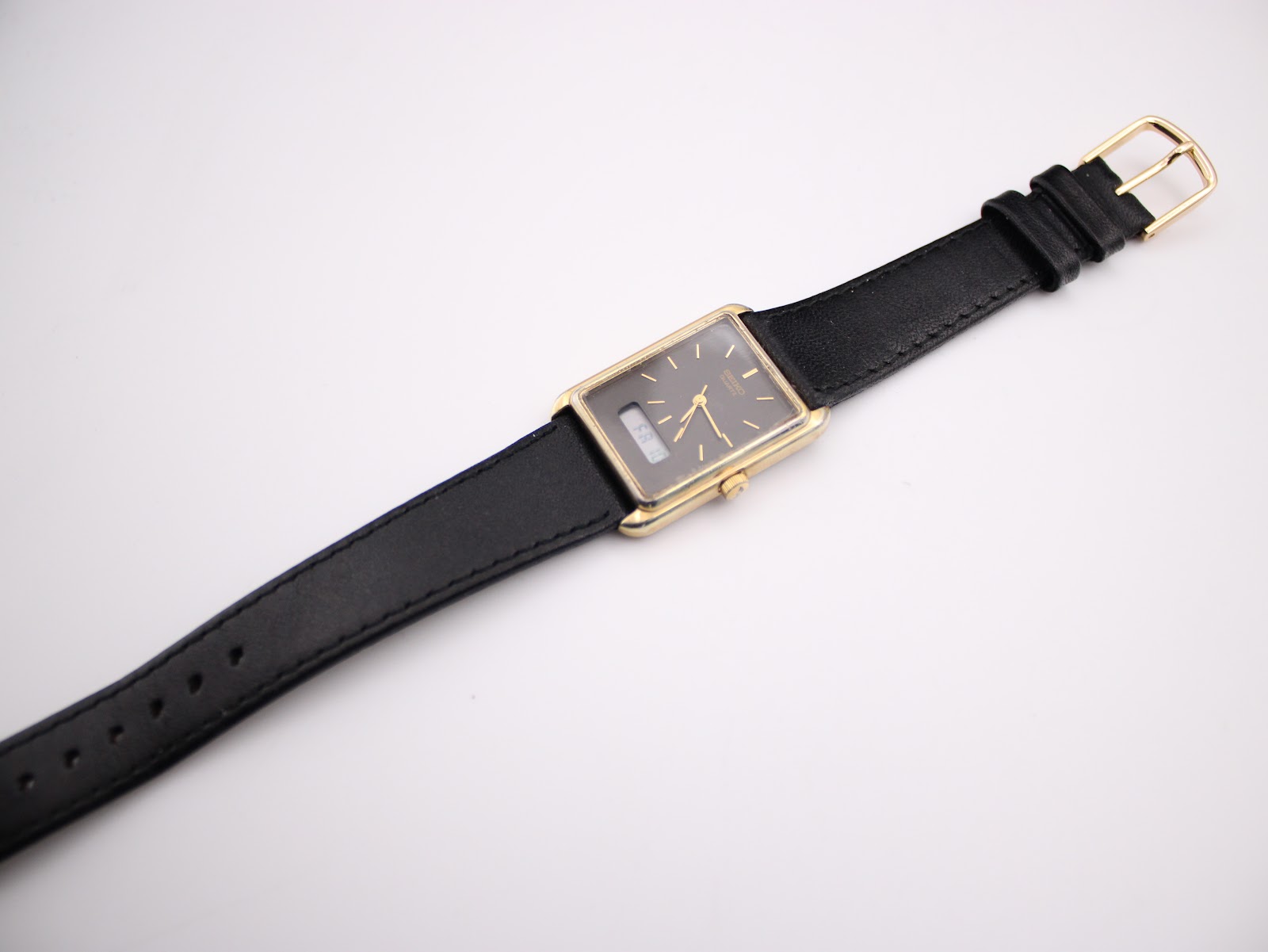 Overhead view of the entire Seiko watch laid flat, displaying the black leather strap with its gold-tone buckle, against a white background.