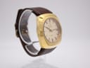 Angled side view of the Certina 288 watch, showing the left side of the gold-plated case, with the brown leather strap on a stand.