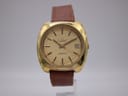 Front view of gold-tone Eterna 407 T watch with textured gold dial and brown leather strap on a stand.