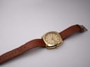 Top-down view of the gold Eterna watch with brown leather strap extended on a white background.