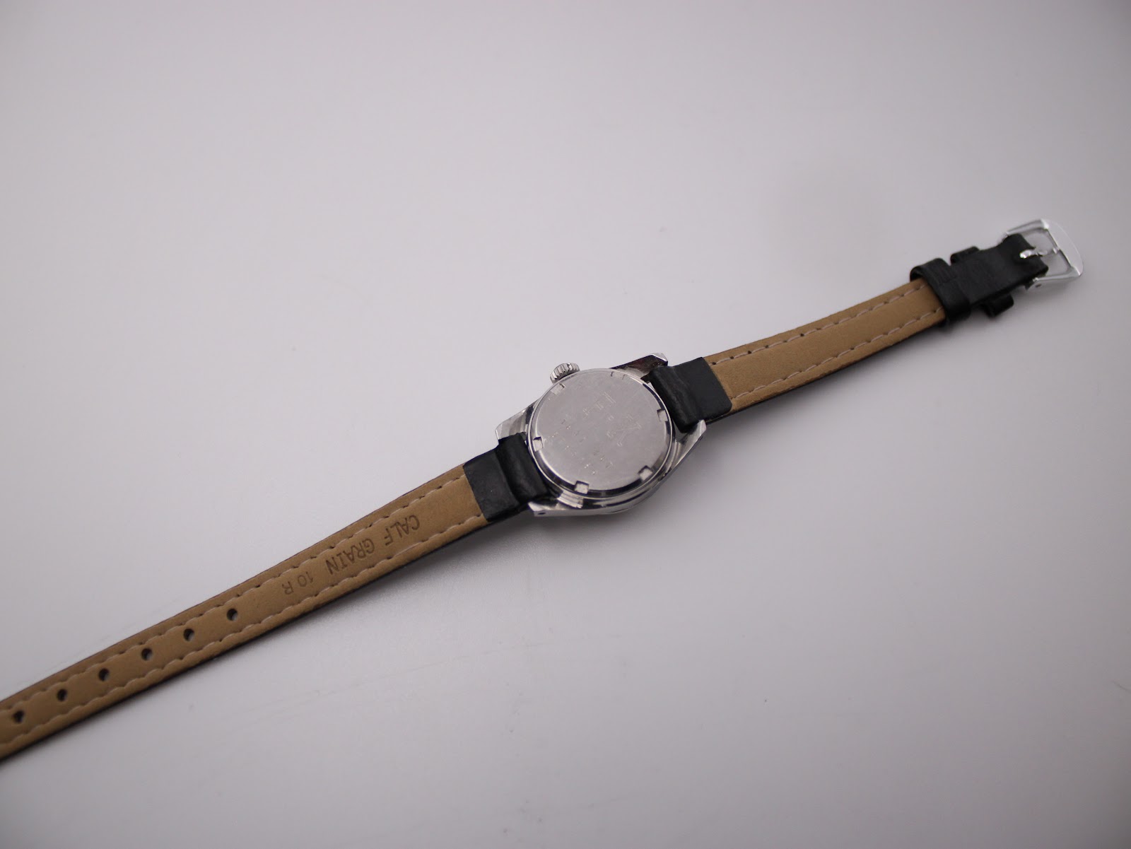 Underside view of the black leather watch strap, showing 'CALF GRAIN 10 R' marking and the silver tone buckle.