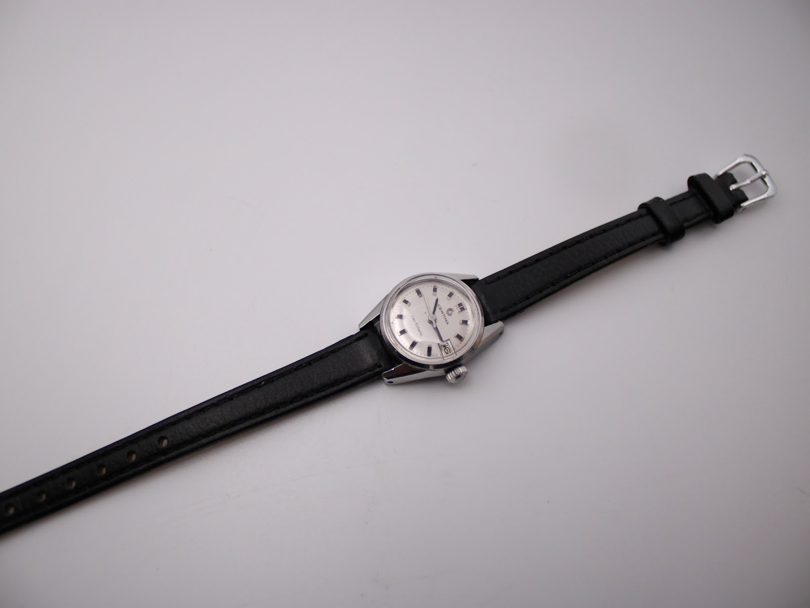 Overhead view of the Certina Certidate watch on its full black leather strap with silver buckle, against a white background.