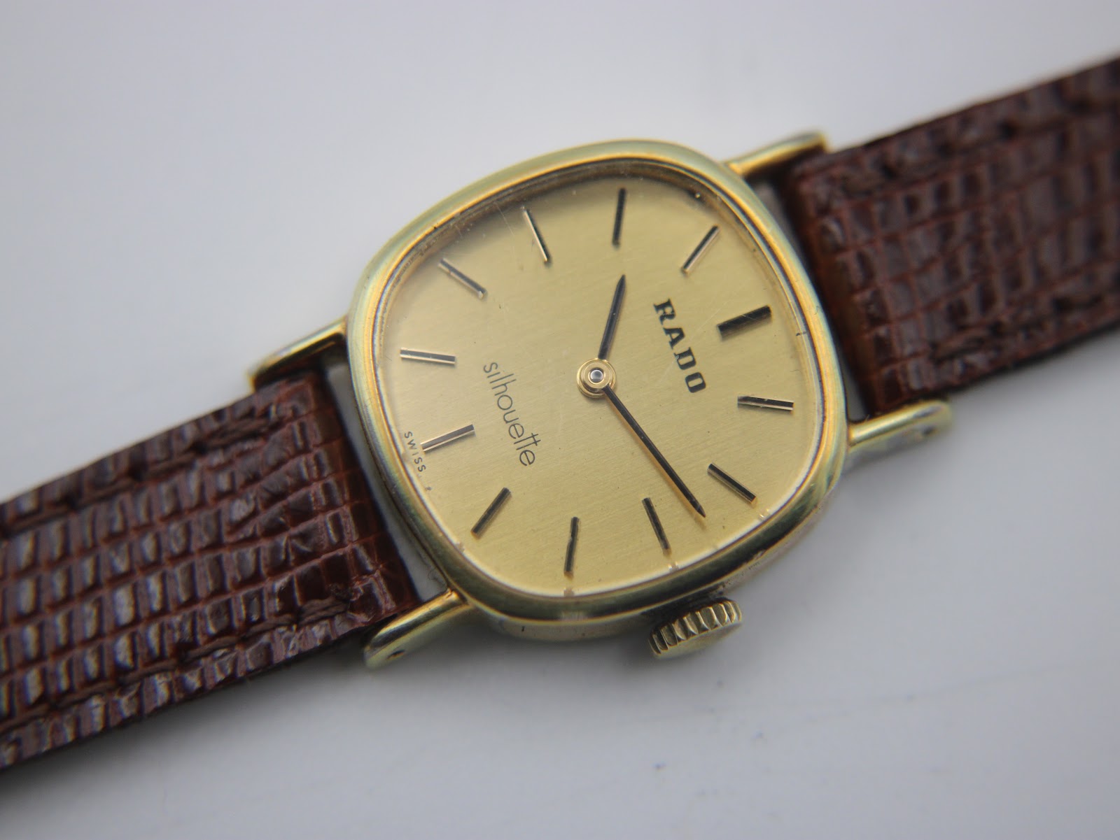 Detailed close-up of the Rado Silhouette gold dial with applied black baton indices, 'RADO' logo, and 'silhouette' text.