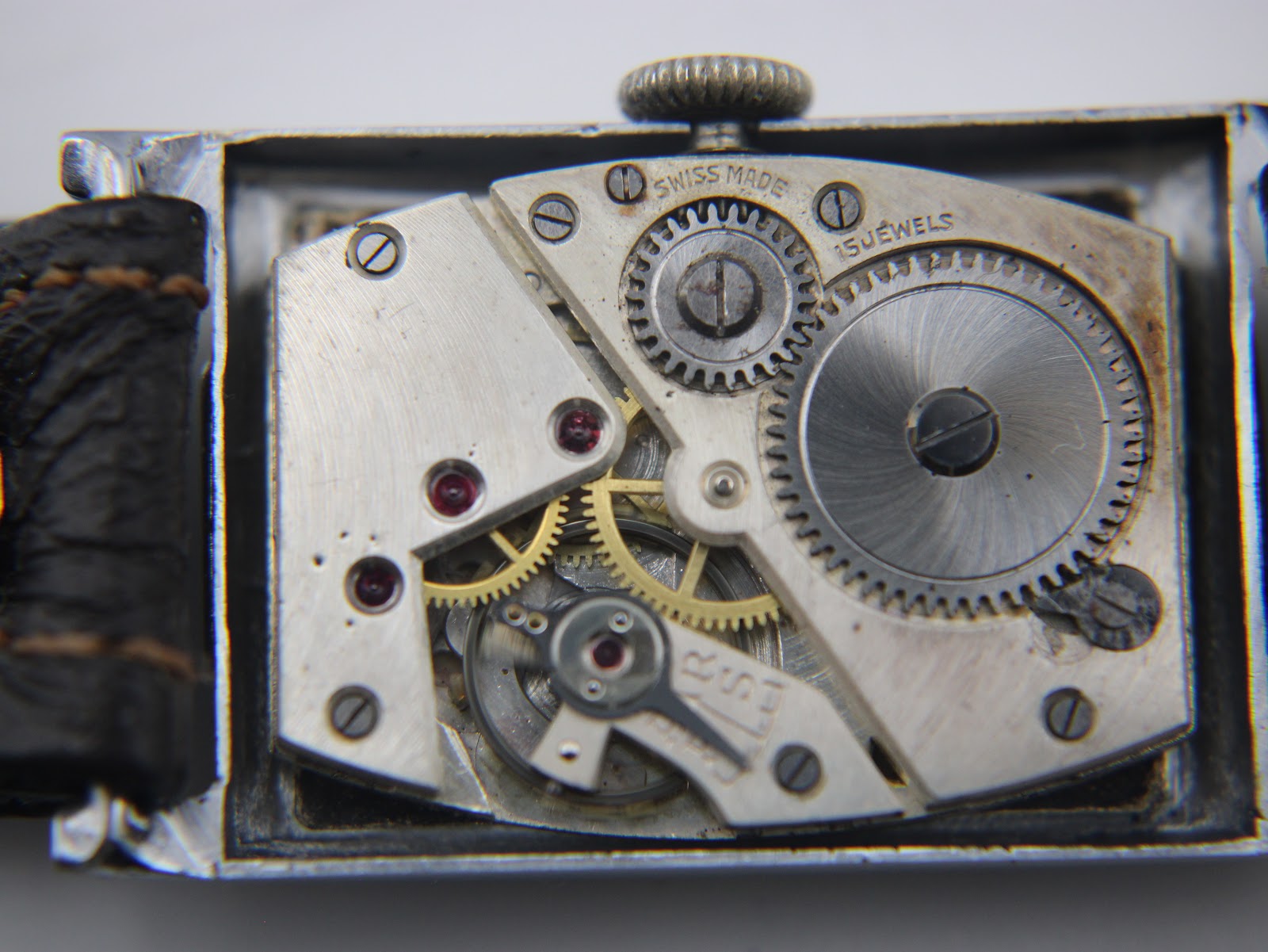 Macro shot of the "SWISS MADE 15 JEWELS" manual wind movement, showing gears and ruby jewels inside the open case.