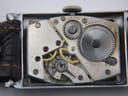 Macro shot of the "SWISS MADE 15 JEWELS" manual wind movement, showing gears and ruby jewels inside the open case.