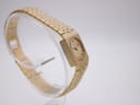 Another angled side view of the gold tone Rotary watch on a clear stand, showing its profile and the continuous design of the bracelet.