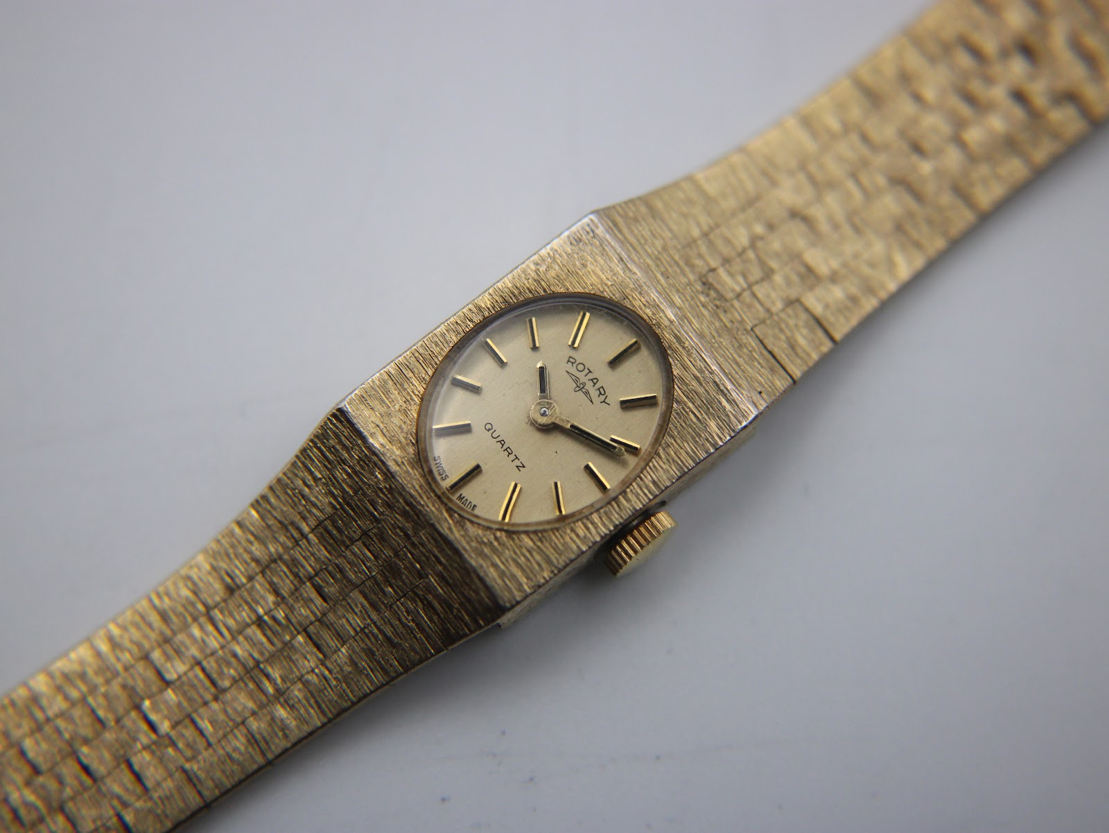 Top-down close-up view of the Rotary watch dial with its cream face, gold baton indices, and the textured integrated gold tone bracelet.