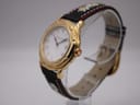 Angled side view of the watch on a display stand, highlighting the profile of the gold tone case and the red Swiss cross crown.