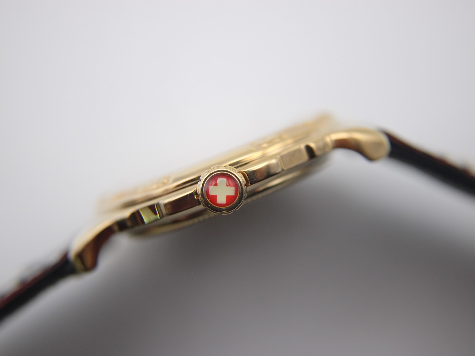 Extreme close-up of the watch crown, featuring a prominent red Swiss cross emblem.