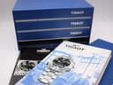 Original Tissot blue box with multiple manuals and papers stacked behind.