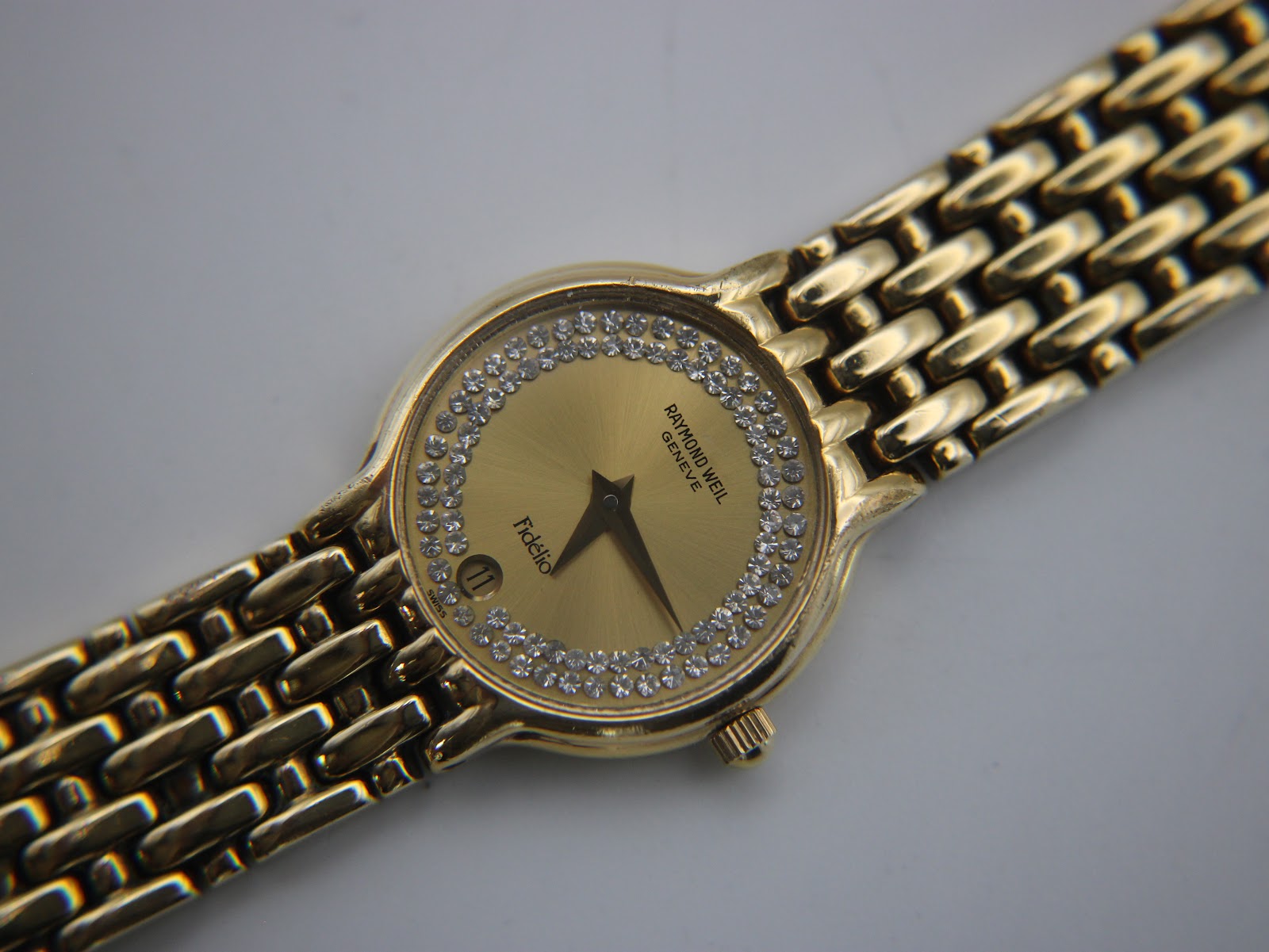 Close-up, slightly angled view of the Raymond Weil Fidelio dial, showing the diamond bezel, gold sunburst dial, and date window.