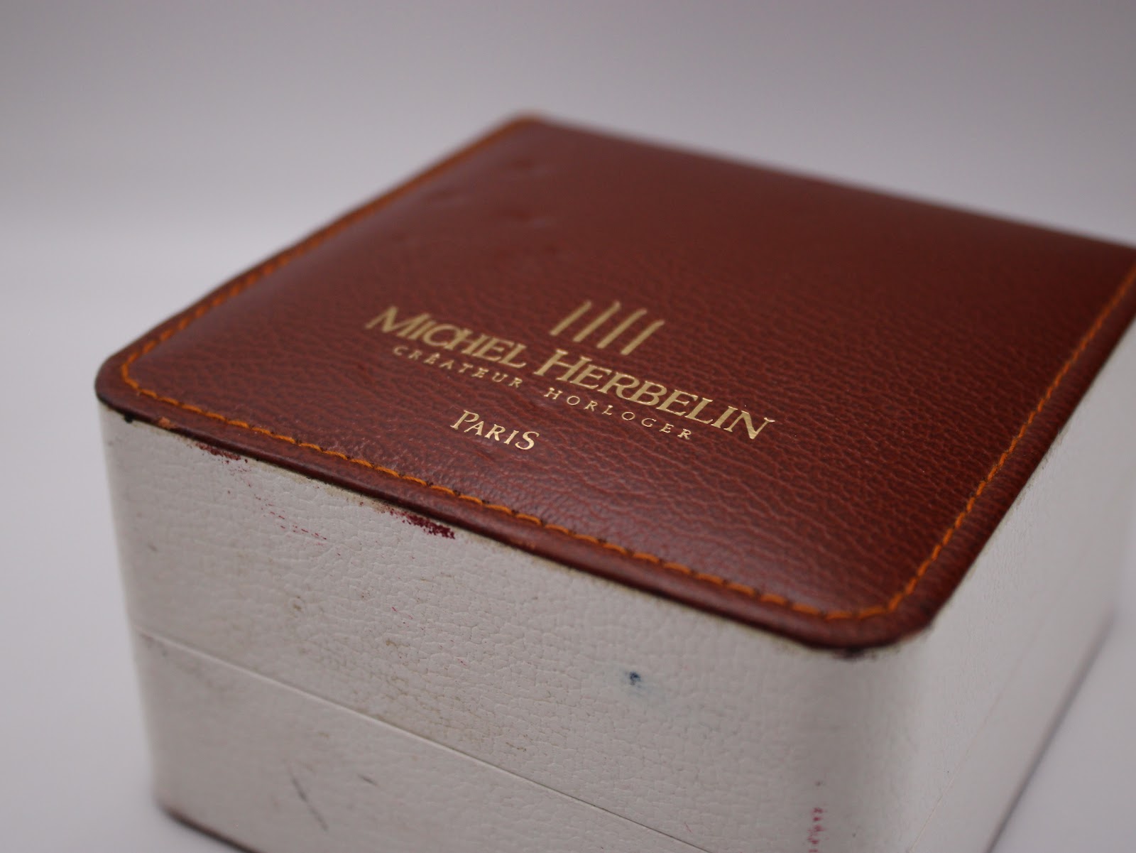 Exterior view of the original Michel Herbelin watch box, featuring a brown faux leather top with gold embossed branding.
