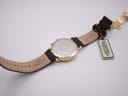 Back view of the watch and strap laid flat, showing the case back with protective film and the interior of the leather strap with branding.