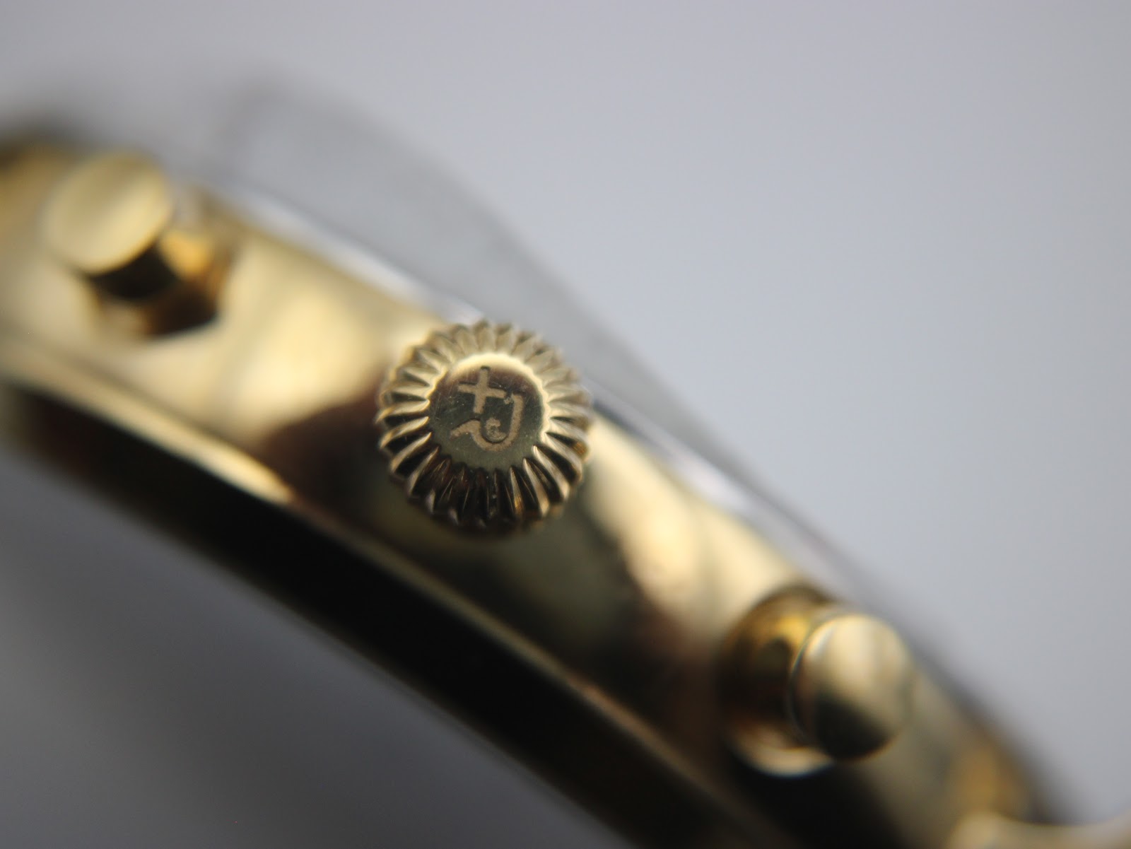 Macro shot of the gold-toned fluted crown with the Roamer 'R' logo engraved on it.