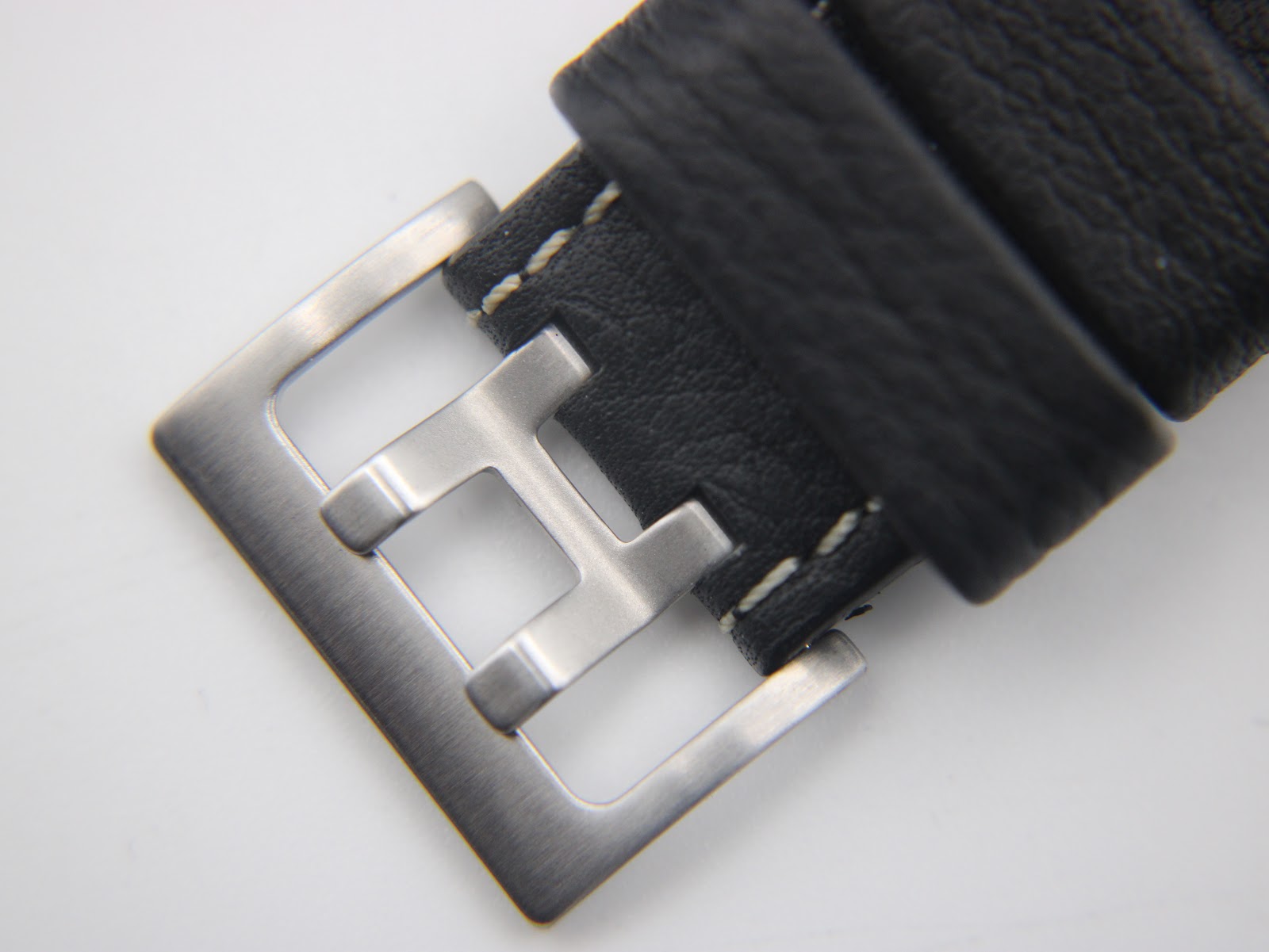 Close-up of the Hamilton branded stainless steel pin buckle on the black leather strap.