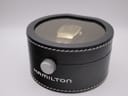 Top view of the original Hamilton watch box, a round black leatherette case with transparent lid.