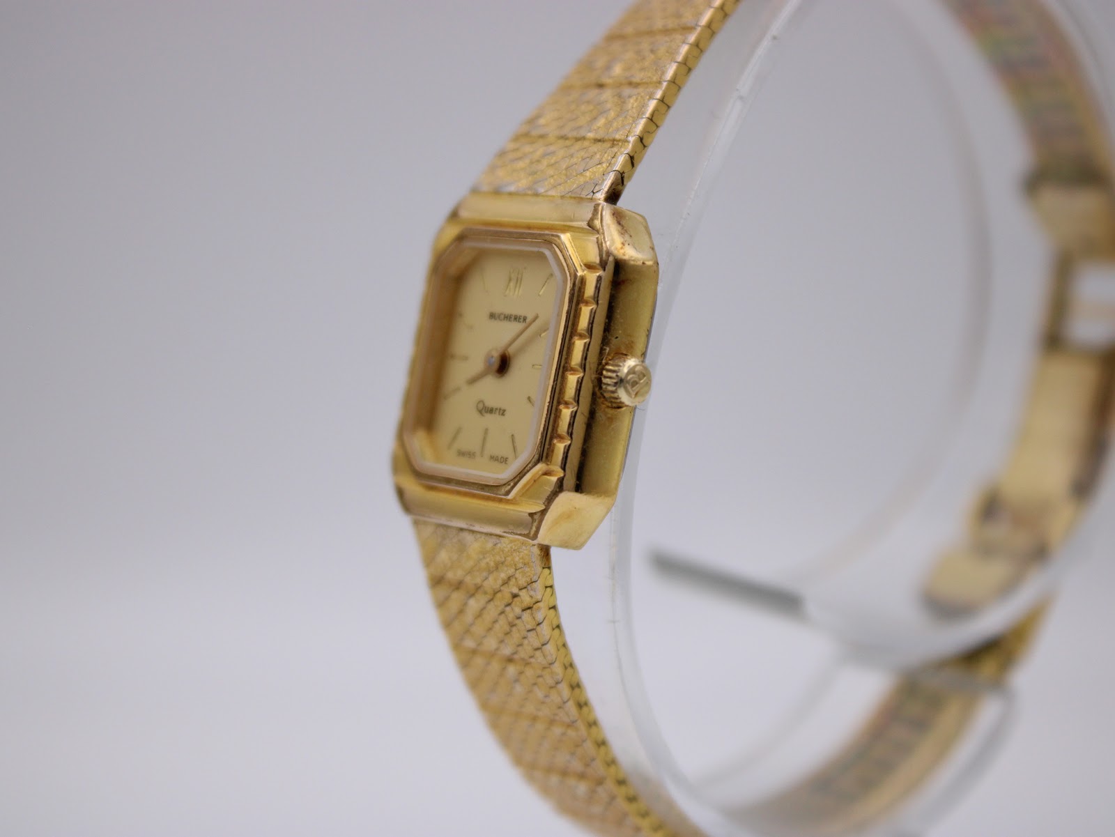Angled side view of the Bucherer watch on a stand, highlighting the gold-tone case and integrated mesh bracelet.