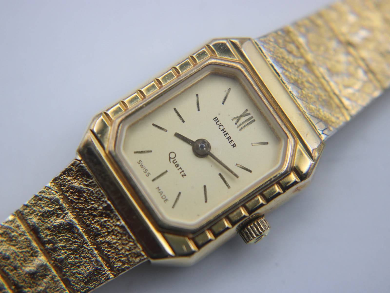 High-angle close-up of the Bucherer watch dial, showing the cream face, Roman numeral XII, and baton indices.