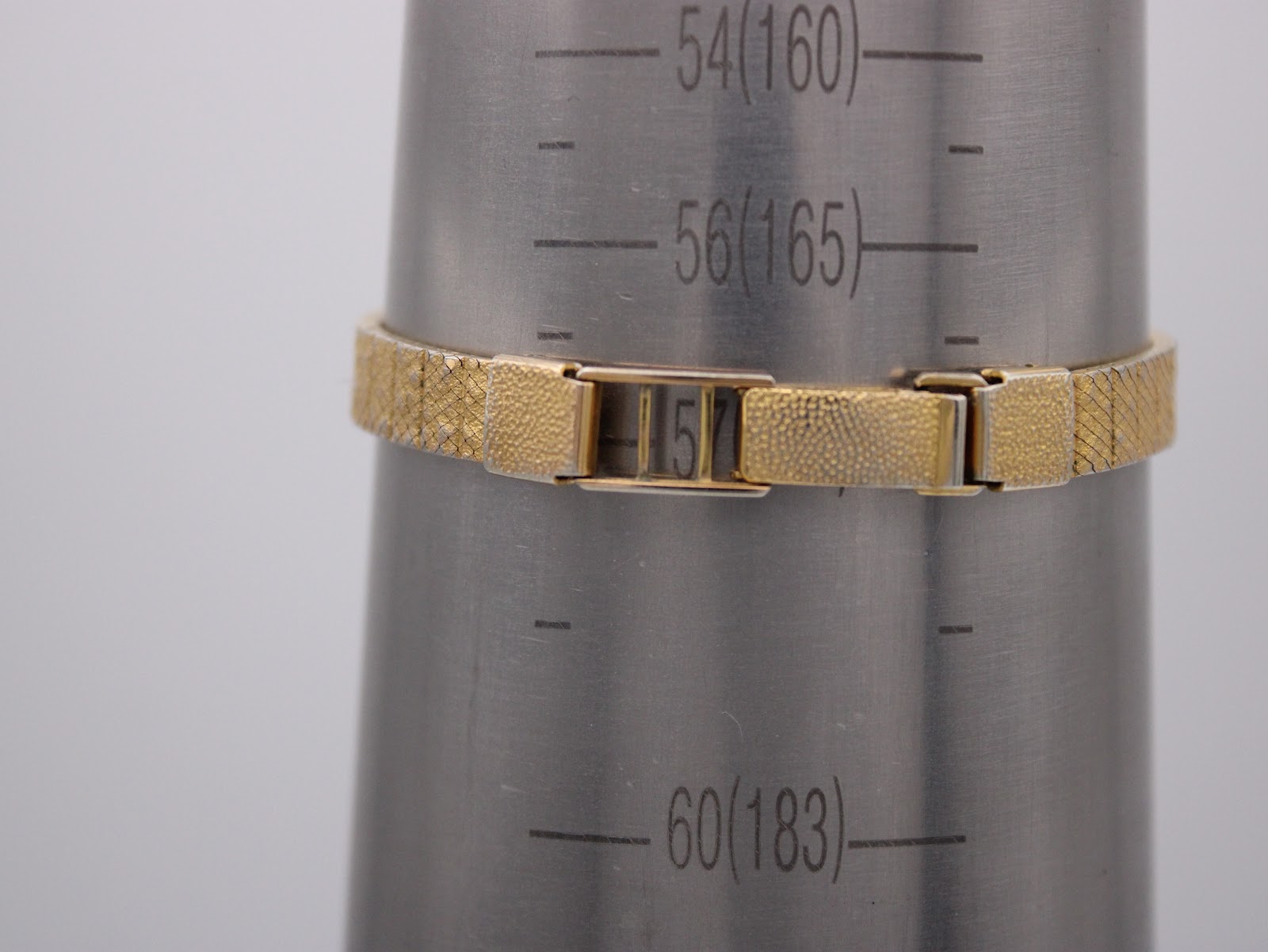 Close-up of the watch clasp and integrated bracelet on a wrist sizing gauge, indicating a wrist circumference of 157mm.