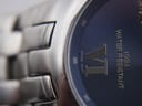 Macro shot of the watch dial edge and case, showing the 'VI' roman numeral, 'SWISS MOVT' text, and the watch's finish.