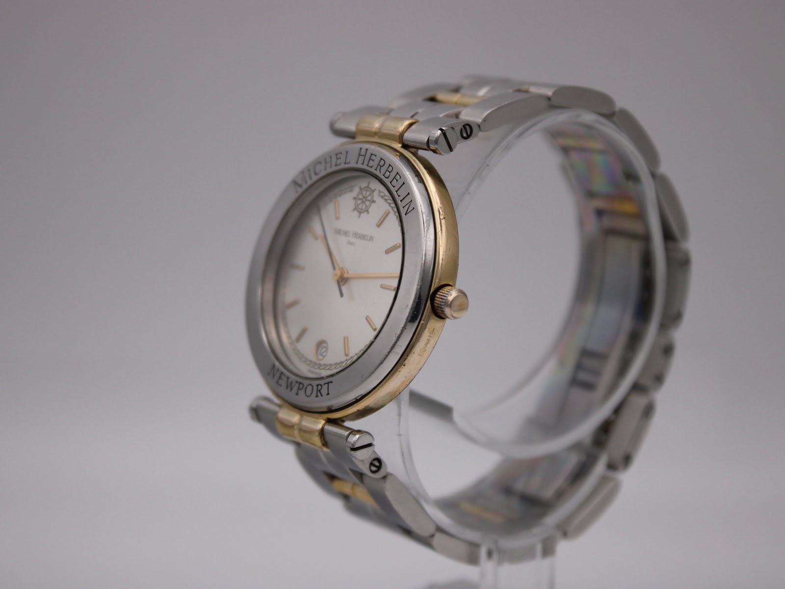 Angled view of the Michel Herbelin Newport watch on a clear display stand, showing the two-tone case and bracelet.