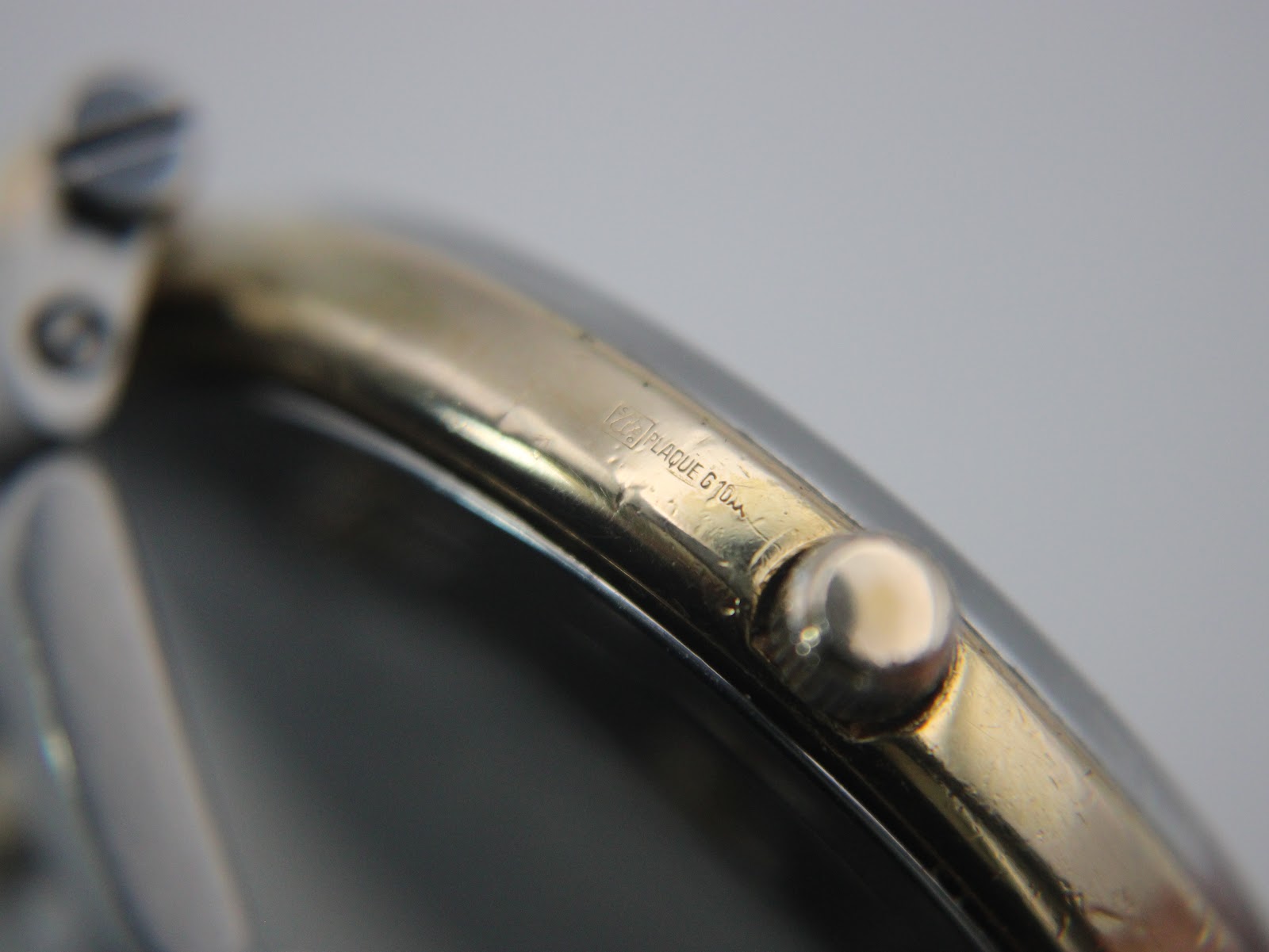 Close-up of the watch case side, showing the crown and a clear "PLAQUE G 10M" engraving indicating 10 micron gold plating.