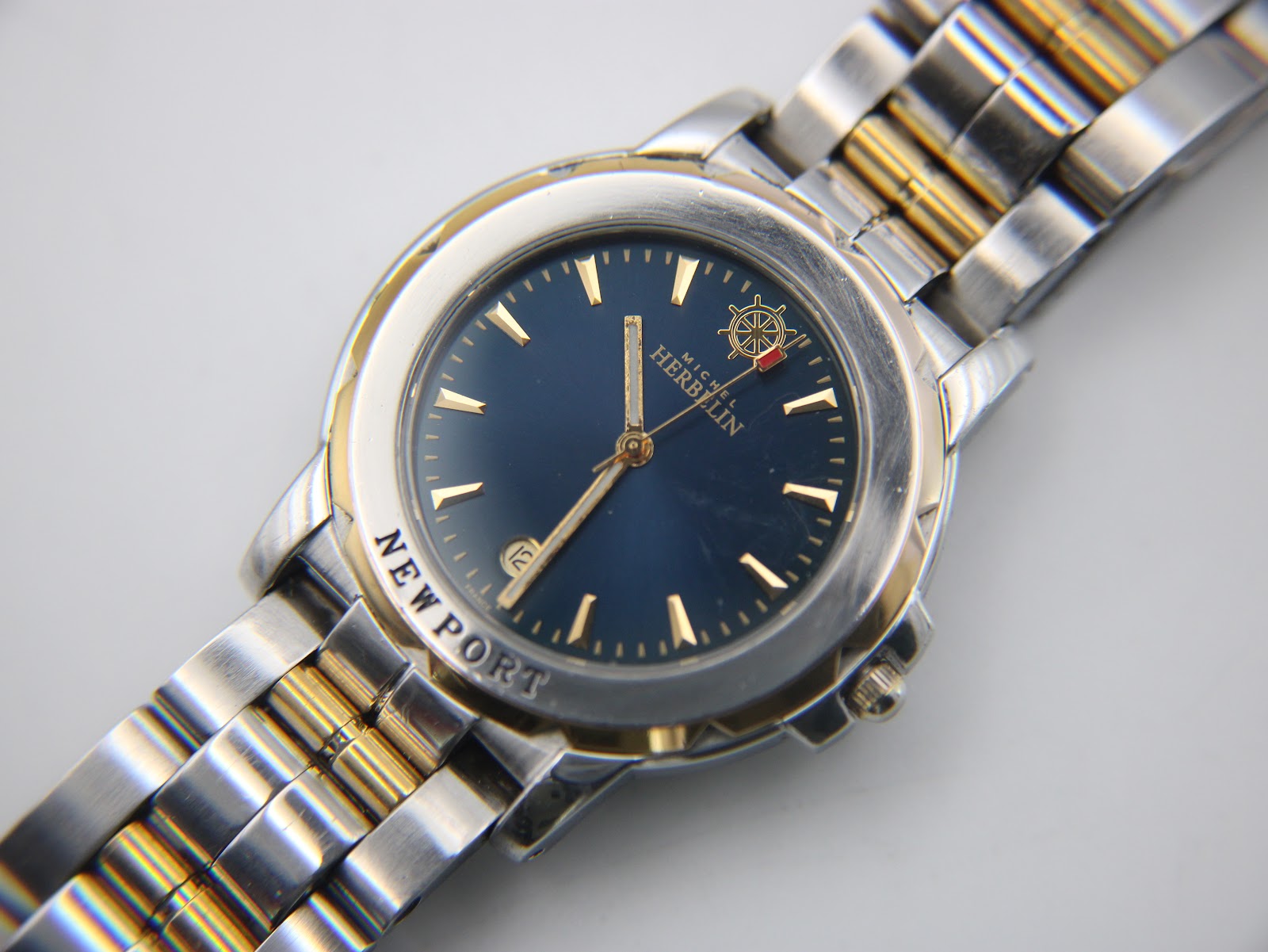 Overhead diagonal shot of the Michel Herbelin Newport, showing the blue dial, date aperture, and the two-tone links of the bracelet.