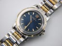 Overhead diagonal shot of the Michel Herbelin Newport, showing the blue dial, date aperture, and the two-tone links of the bracelet.