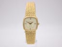 Front view of the gold-plated Certina quartz watch, showing its rectangular cushion case, champagne dial with Roman numerals, and integrated gold mesh bracelet on a clear display stand.