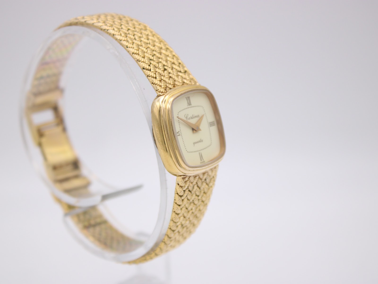 Another angled side view of the Certina watch, showing more of the gold mesh bracelet as it curves around the display stand.