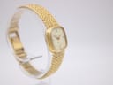 Another angled side view of the Certina watch, showing more of the gold mesh bracelet as it curves around the display stand.