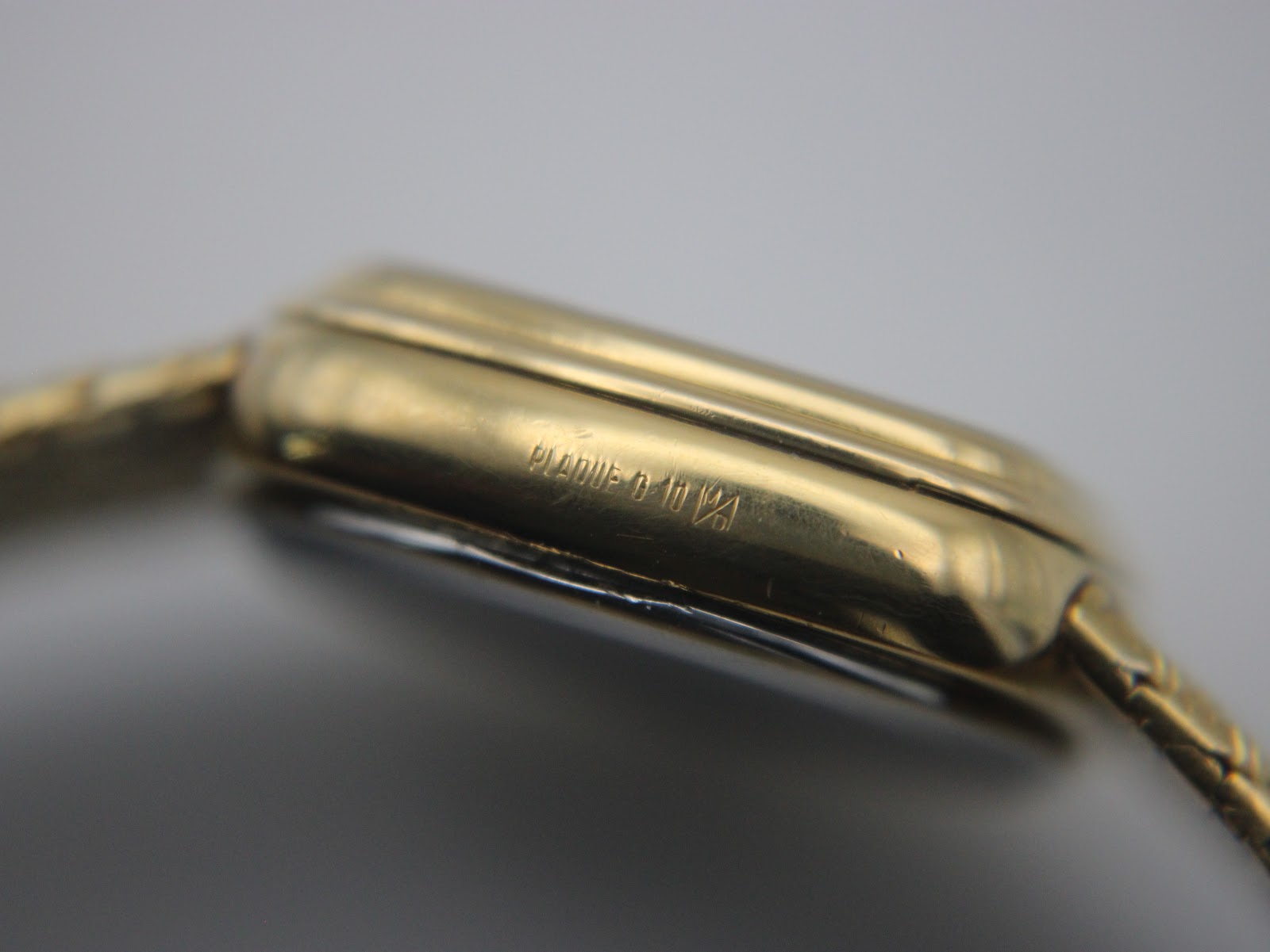 Detailed side view of the watch case, showing an engraving 'PLAQUE G 10M' indicating 10-micron gold plating, with some minor wear visible.