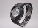 Side view of black Casio G-Shock GA-110C watch on a clear stand, showing mode buttons and textured resin case.