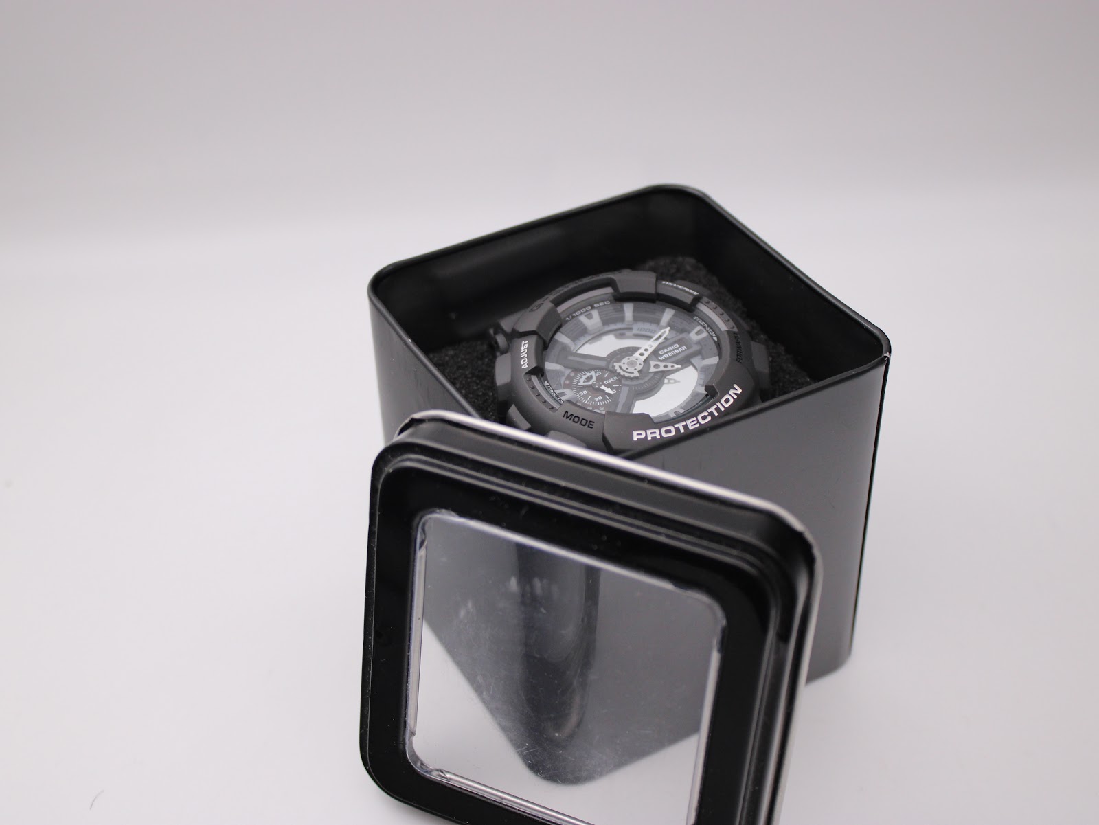Casio G-Shock GA-110C watch sitting in an open black metal tin with a clear lid.