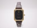 Front view of the Maurice Lacroix 71570 watch with rectangular gold-tone case, black dial, and brown leather strap on a white background.