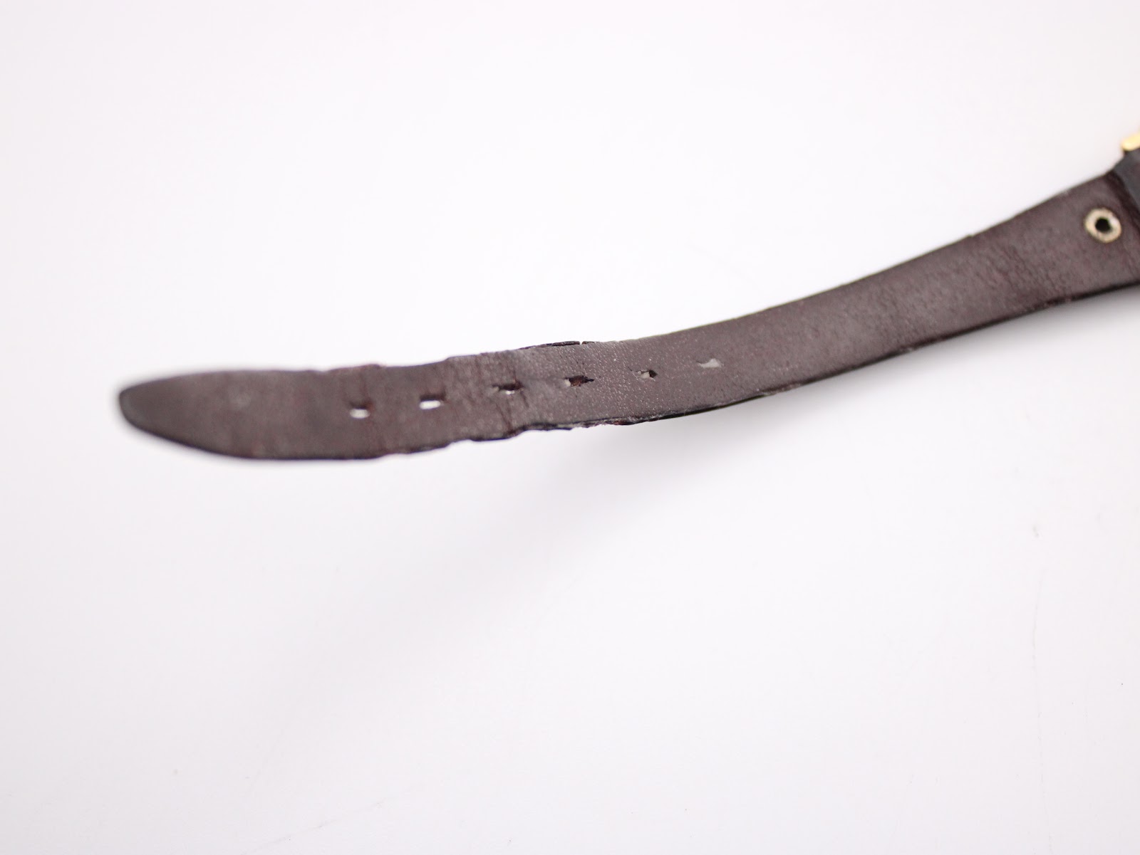 Close-up detail of the worn end of the brown leather strap, revealing visible creasing and slight damage around the buckle holes.