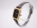 Angled view of the Maurice Lacroix watch on a clear display stand, showing the crown, side profile, and gold-tone case.