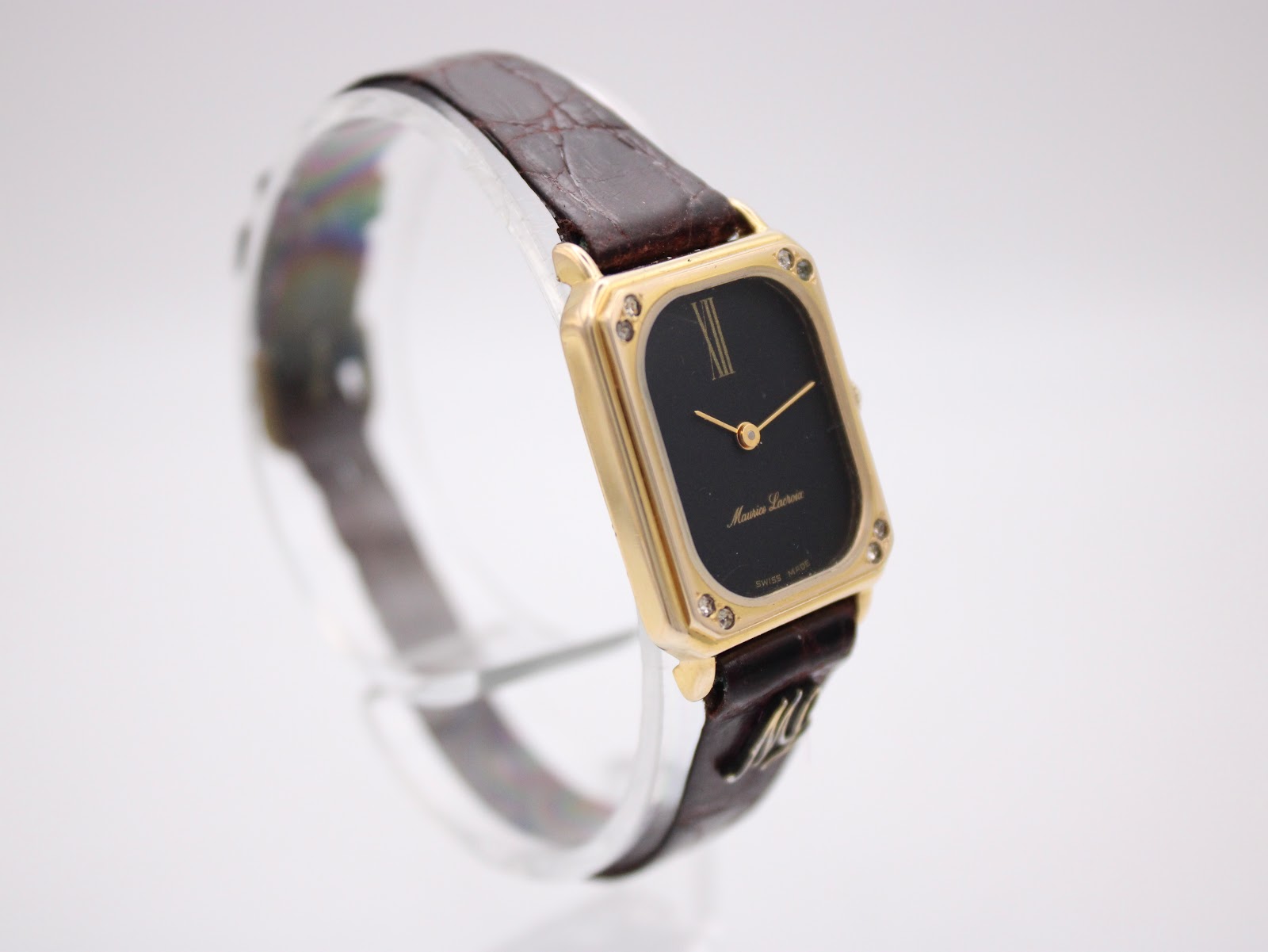 Another angled view of the Maurice Lacroix watch on a clear display stand, highlighting the rectangular case and black dial with gold accents.