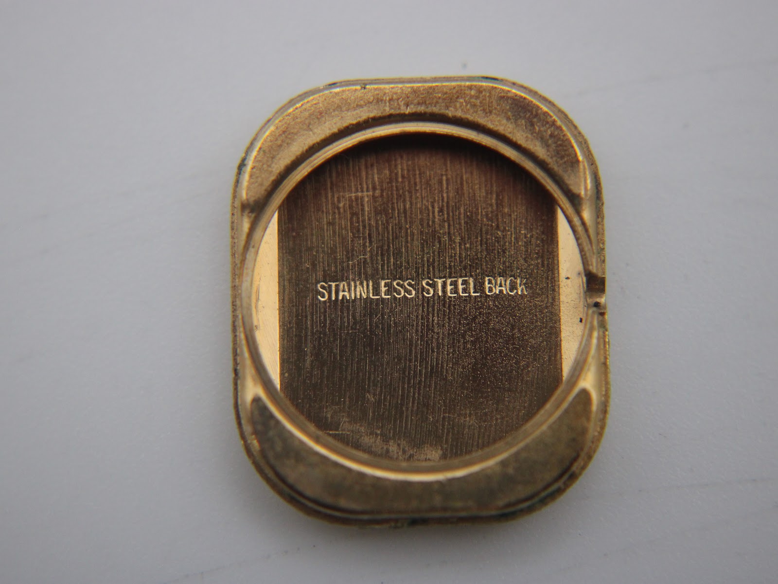 Interior view of the watch case back, showing the 'Stainless Steel Back' engraving and gold-toned finish.
