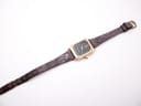 Full length top-down view of the watch and its worn brown leather strap with a gold-tone buckle, against a plain white background.