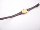 Full length back view of the watch, showing the gold-tone case back, the entire length of the leather strap, and its adjustment holes.