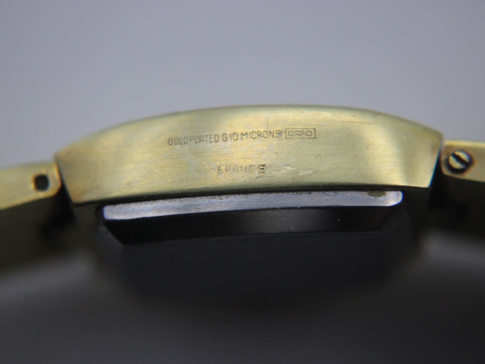 Close-up of the watch case side, showing engraved text 'GOLDPLATED G10 MICRONS' and 'FRANCE'.