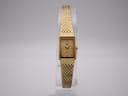 Front view of the gold tone Rotary rectangular quartz watch on a clear stand, showcasing the mesh bracelet.