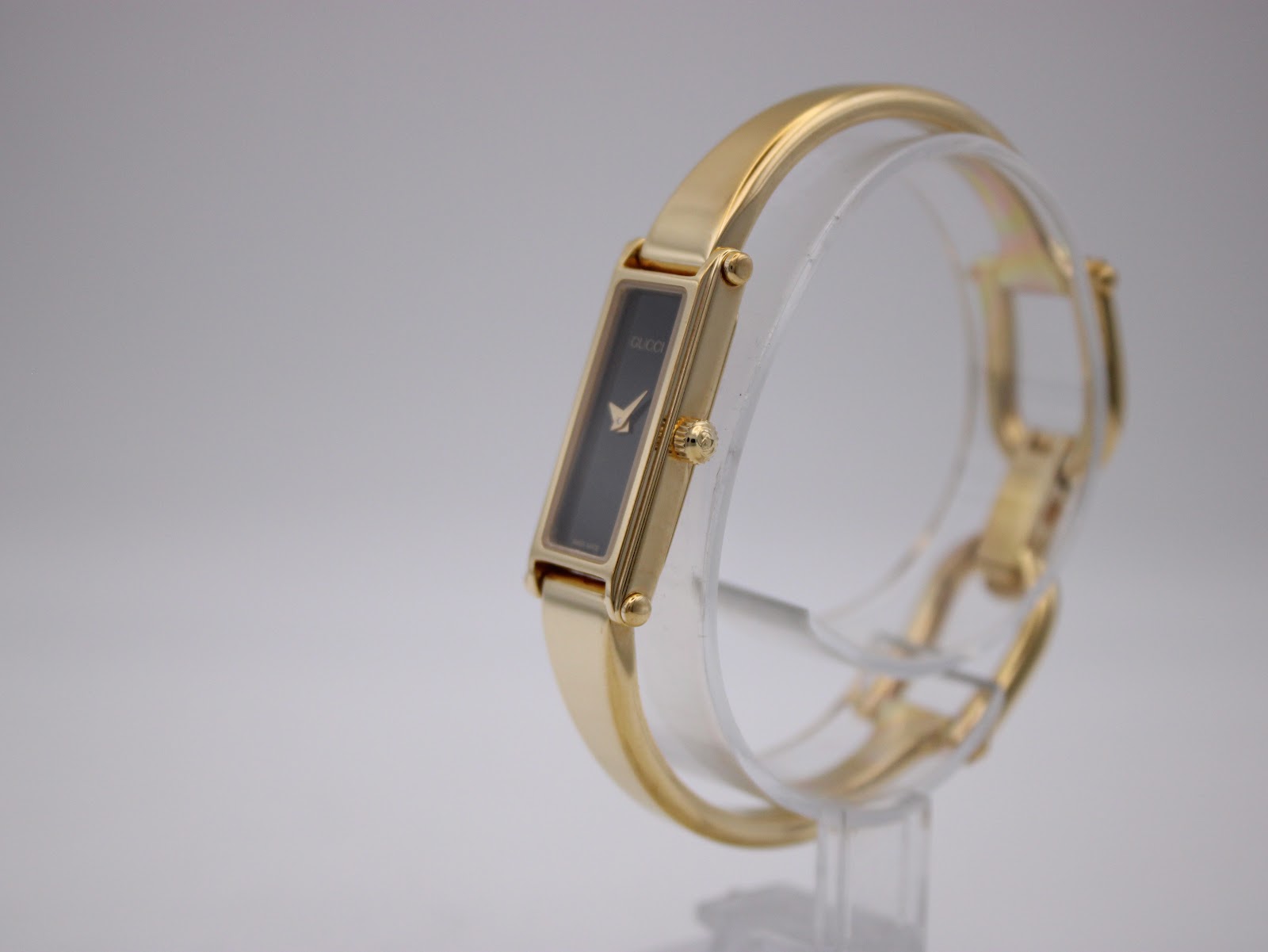 Angled side view of Gucci 1500L watch on a clear display stand, showing the crown and integrated bangle bracelet.