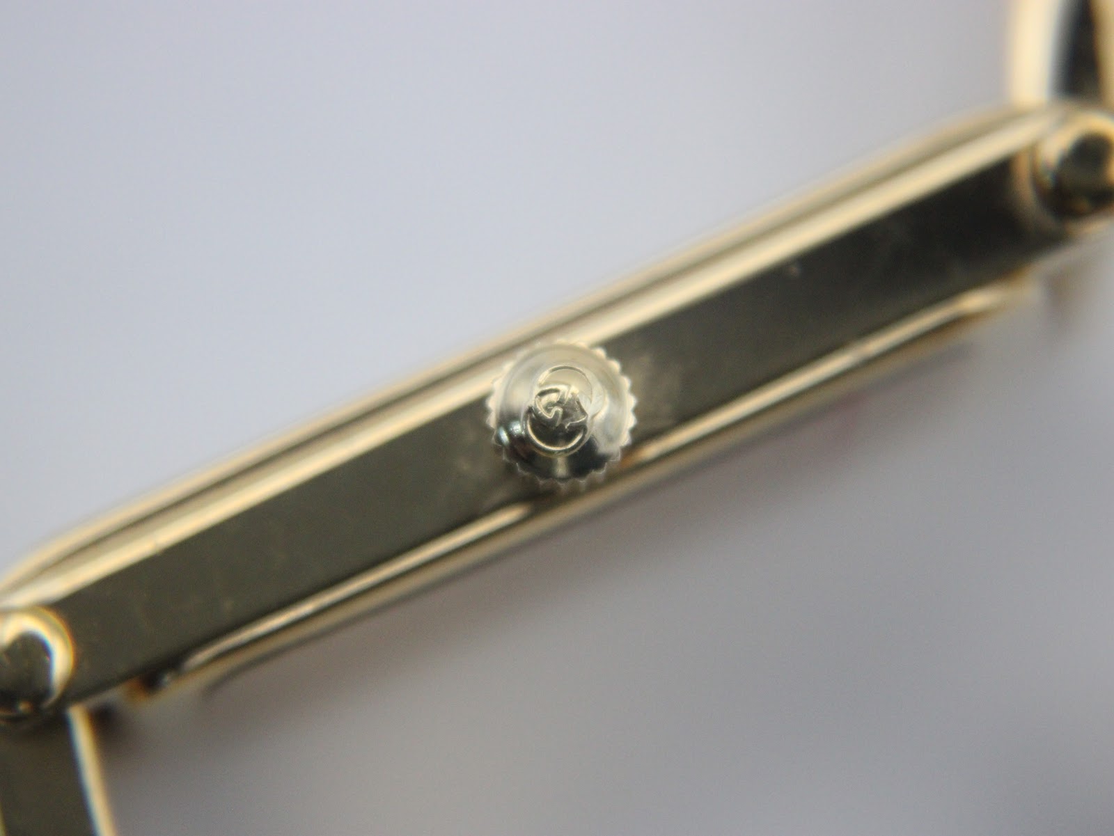 Close-up of the gold-tone watch crown, featuring a subtle 'G' logo embossed on its face.