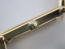 Close-up of the gold-tone watch crown, featuring a subtle 'G' logo embossed on its face.